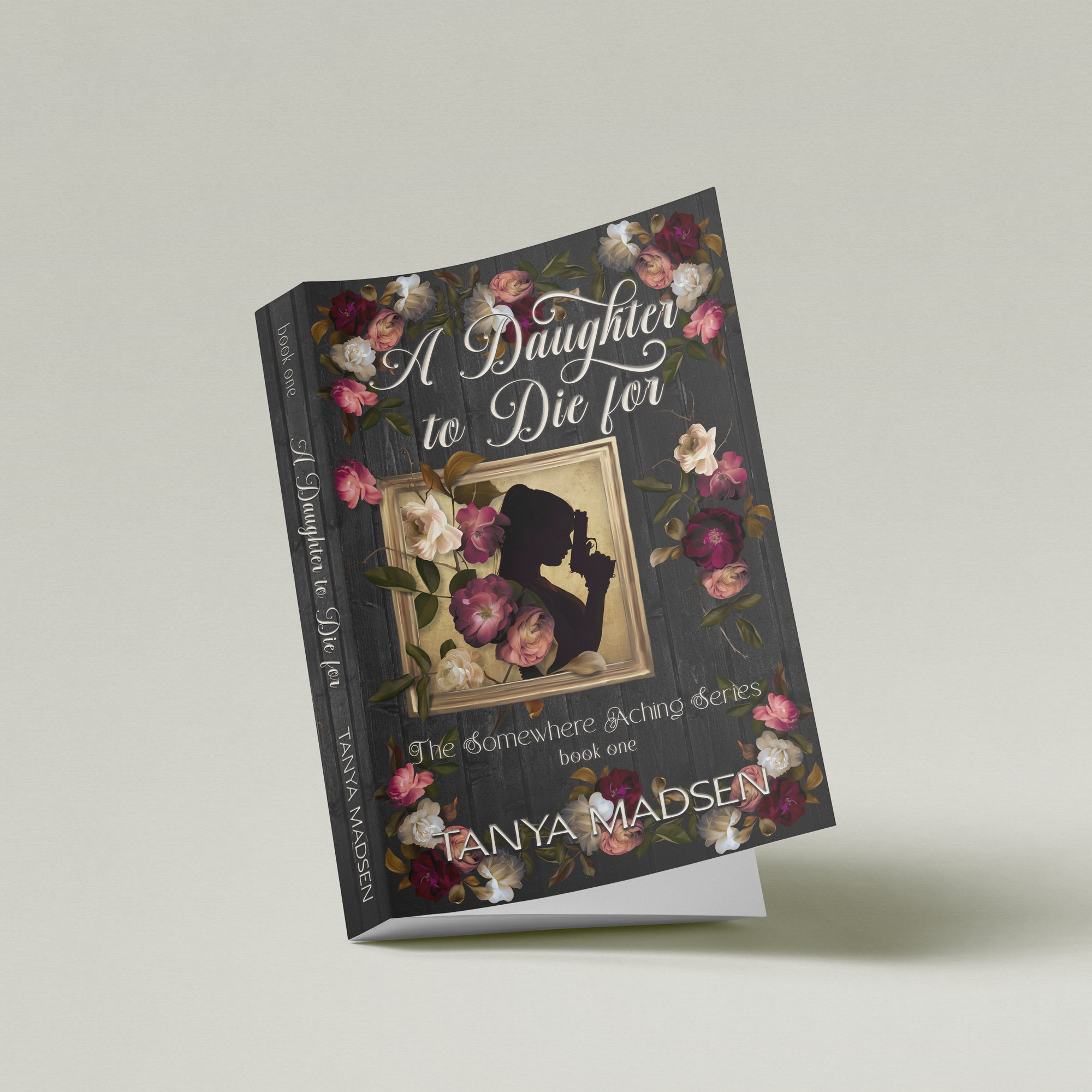 A side-view image of the book A Daughter to Die For, surrounded by a floral design. The cover shows a silhouette of a daughter holding a gun with her head bowed. The book is set against a sage‑green background.