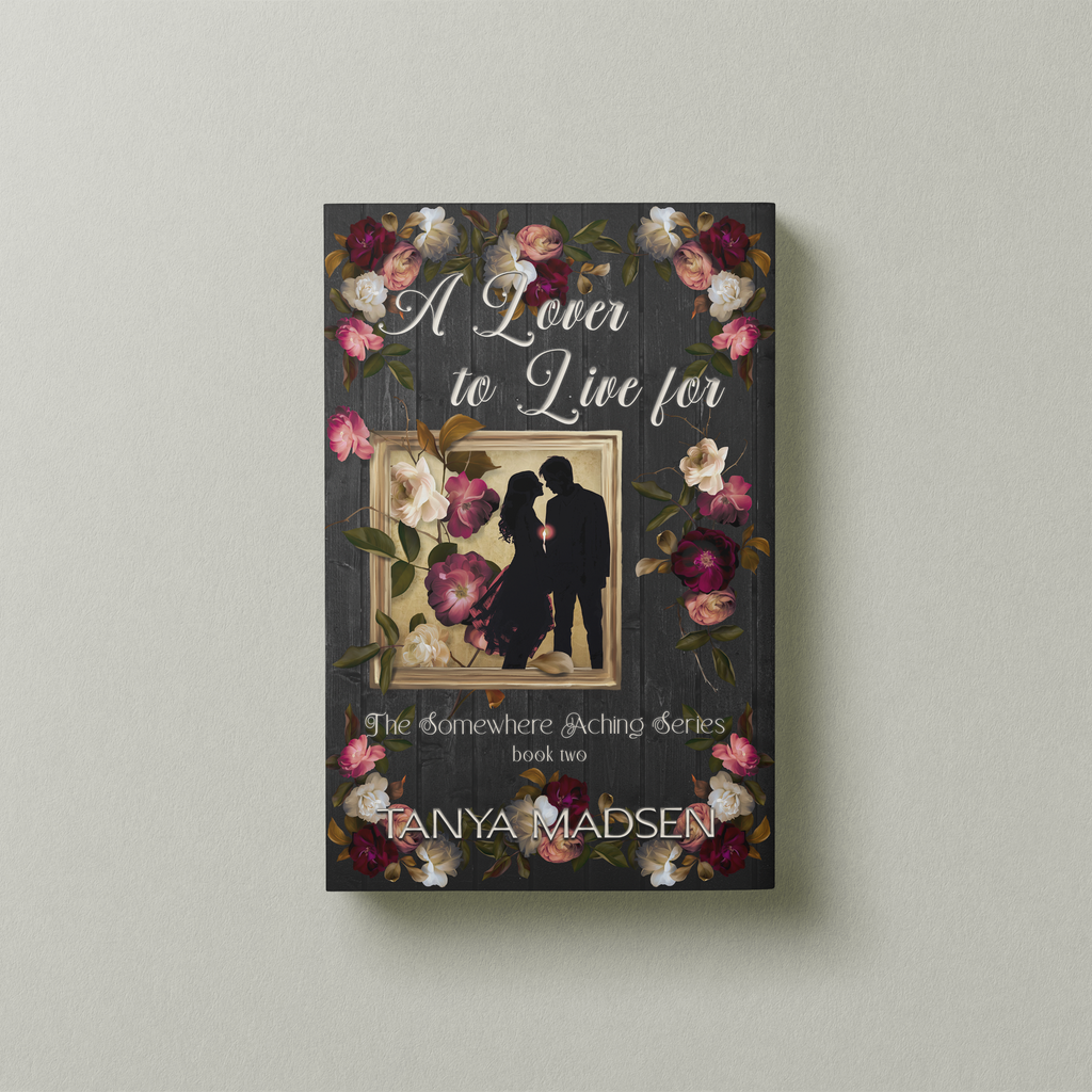 A front‑facing image of the book A Lover to Live For, surrounded by a floral design. The cover shows a silhouette of a couple almost kissing, the sun peaking between them. The book is set against a sage‑green background.