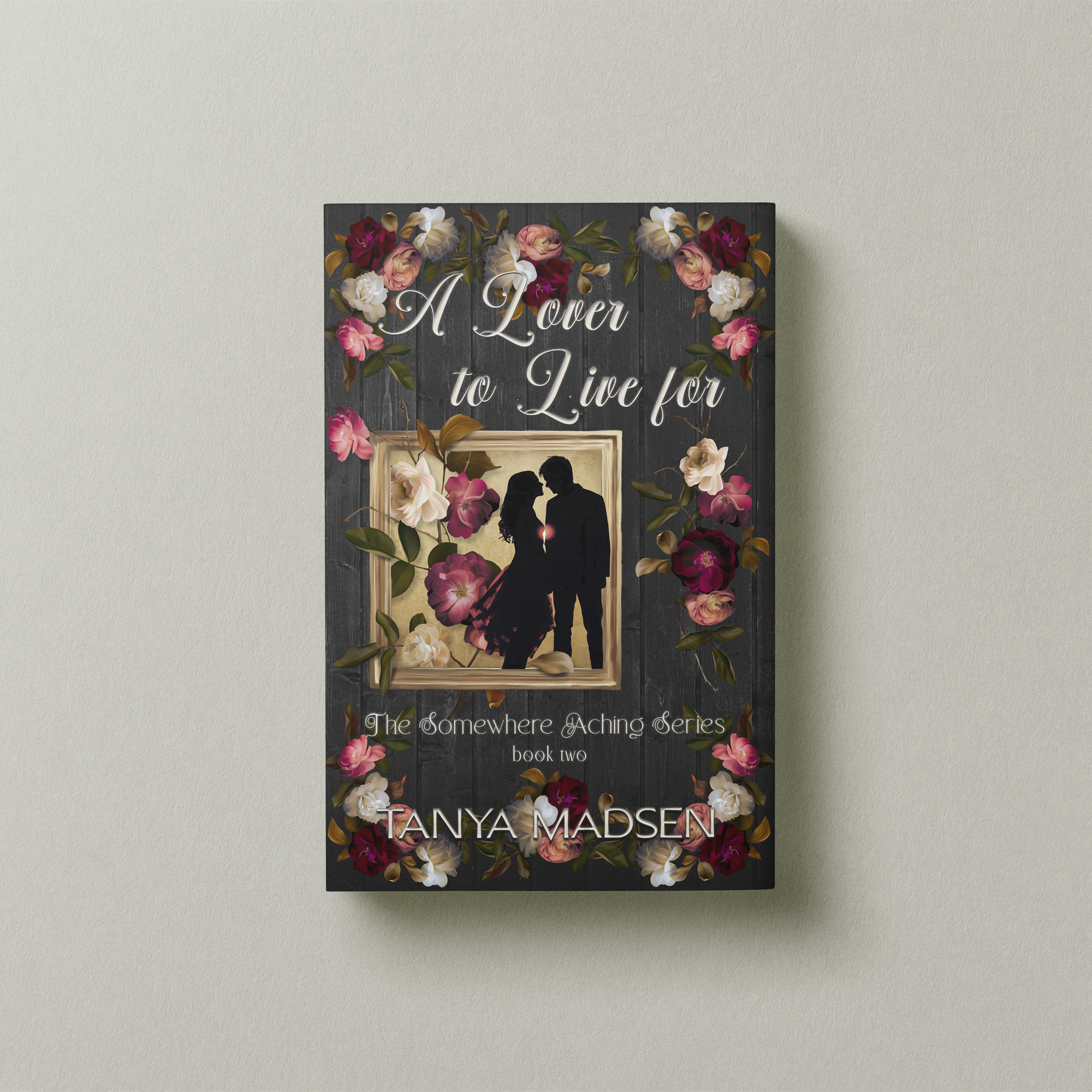 A front‑facing image of the book A Lover to Live For, surrounded by a floral design. The cover shows a silhouette of a couple almost kissing, the sun peaking between them. The book is set against a sage‑green background.
