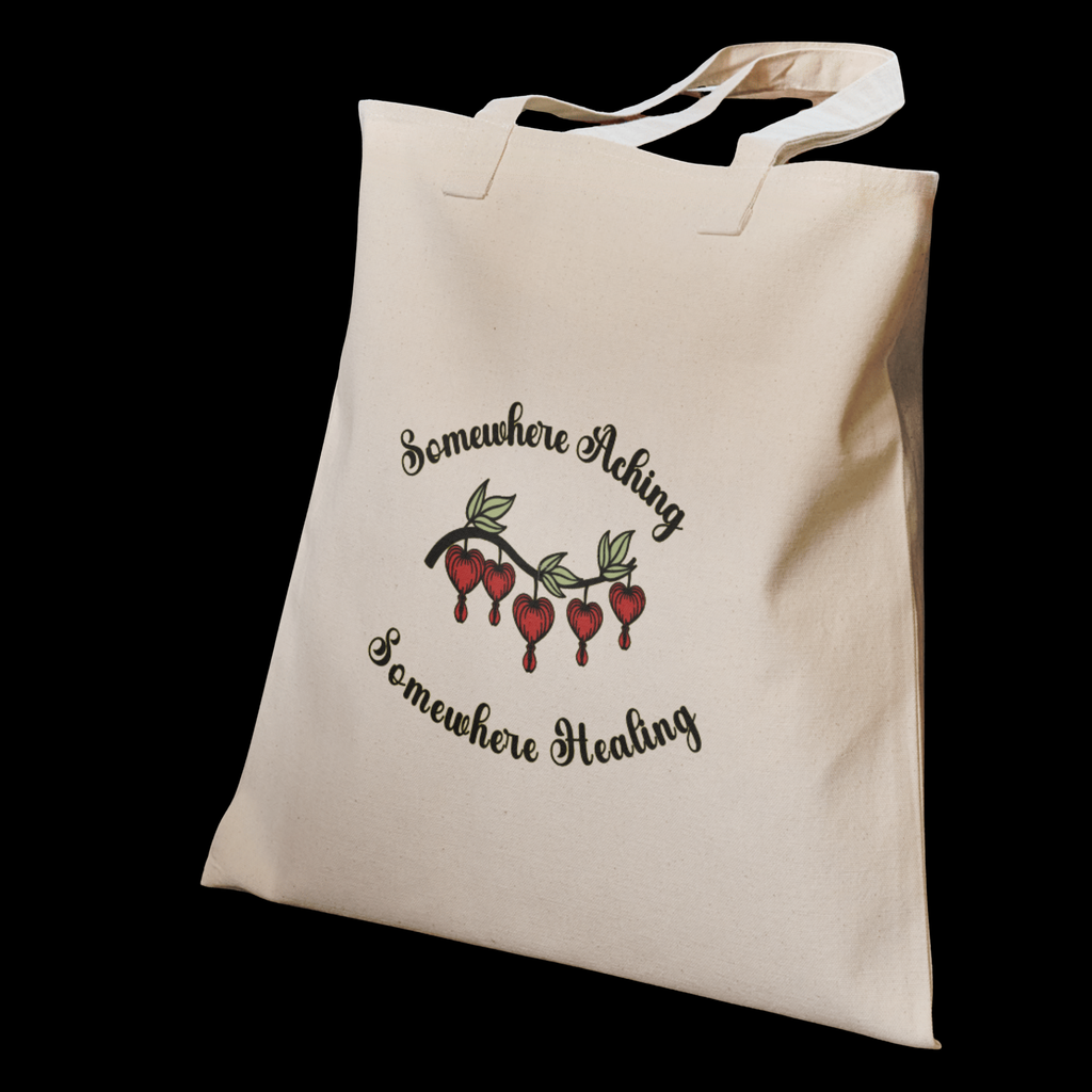A canvas tote illustrated with the quote “Somewhere Aching, Somewhere Healing” paired with a cluster of bleeding hearts.