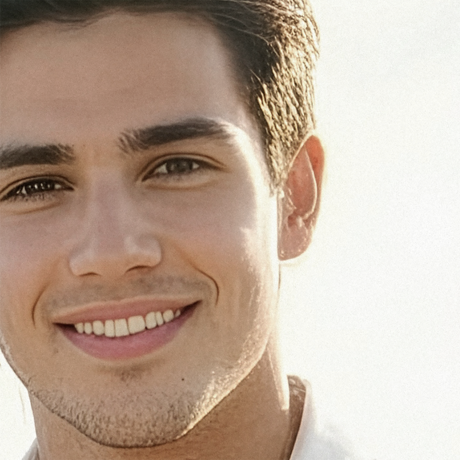 A close-up photo of Nicolas smiling at the camera, his dark eyes sparkling, standing in front of the ocean.