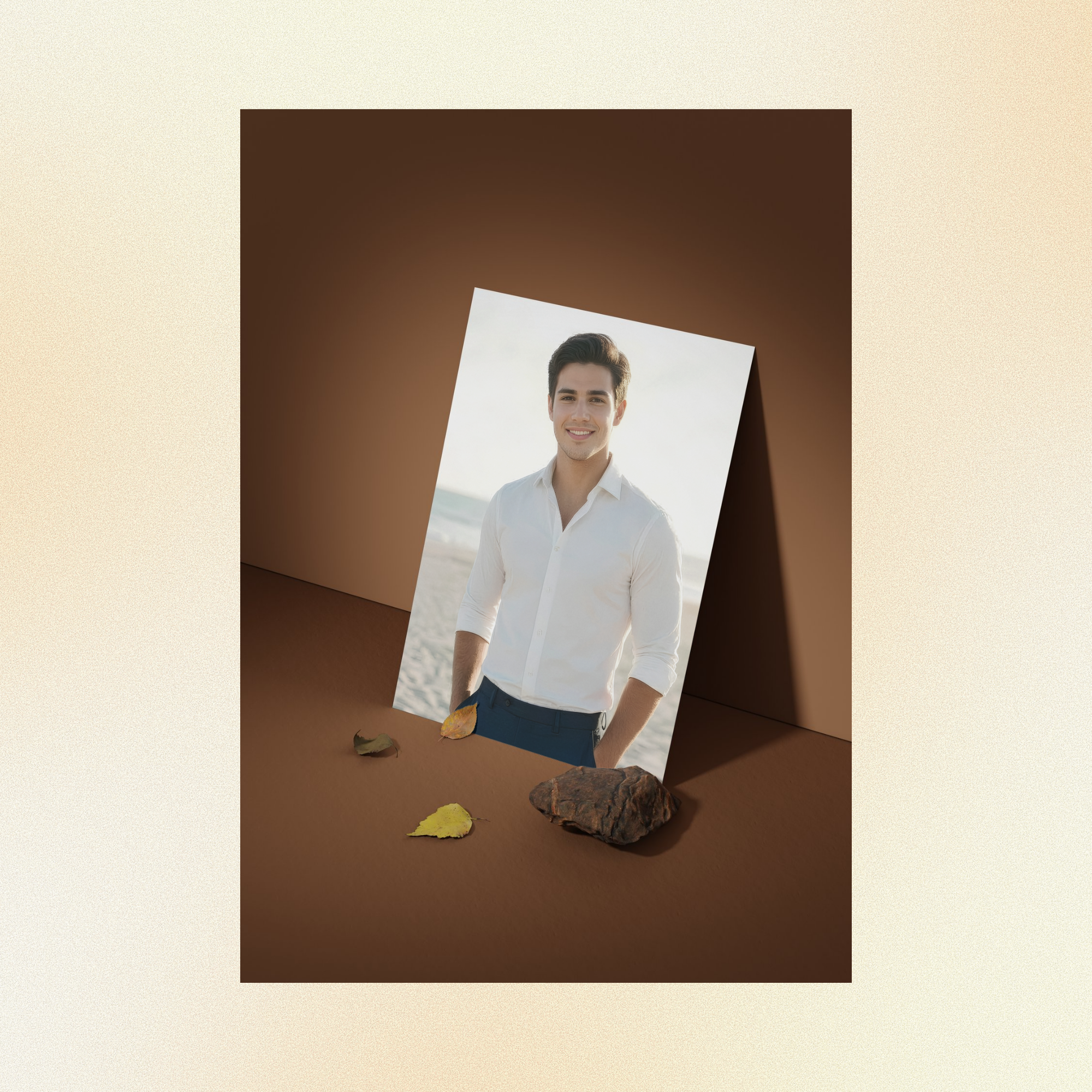 A photo of Nicolas displayed against a brown wall, smiling at the camera, hands in his pockets his dark eyes sparkling, standing casually in front of the ocean wearing a white dress shirt and dark blue slacks.