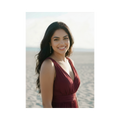 A soft-toned photo of Judith smiling at the camera, her green eyes sparkling, standing in front of the ocean wearing a burgundy dress.