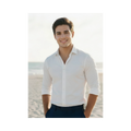 A soft-toned photo of Nicolas smiling at the camera, hands in his pockets his dark eyes sparkling, standing casually in front of the ocean wearing a white dress shirt and dark blue slacks.