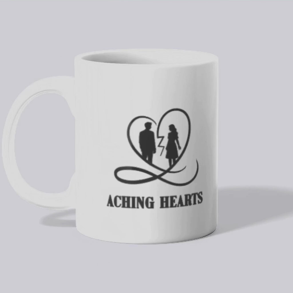 A mockup of the Aching Hearts mug featuring black and white graphics with text "love hurts before it heals" and the aching hearts logo of a man and woman inside of a cracked heart on a white background.